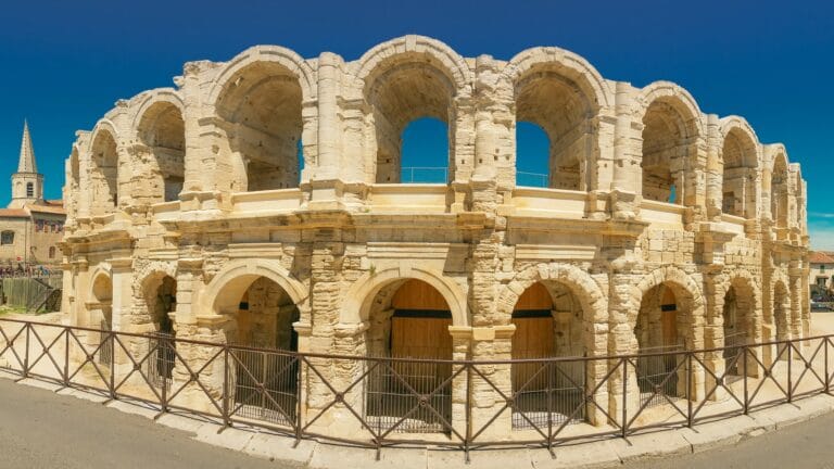 A view from the street of the ruins of the Roman amphitheatre in Arles on a bright sunny day.