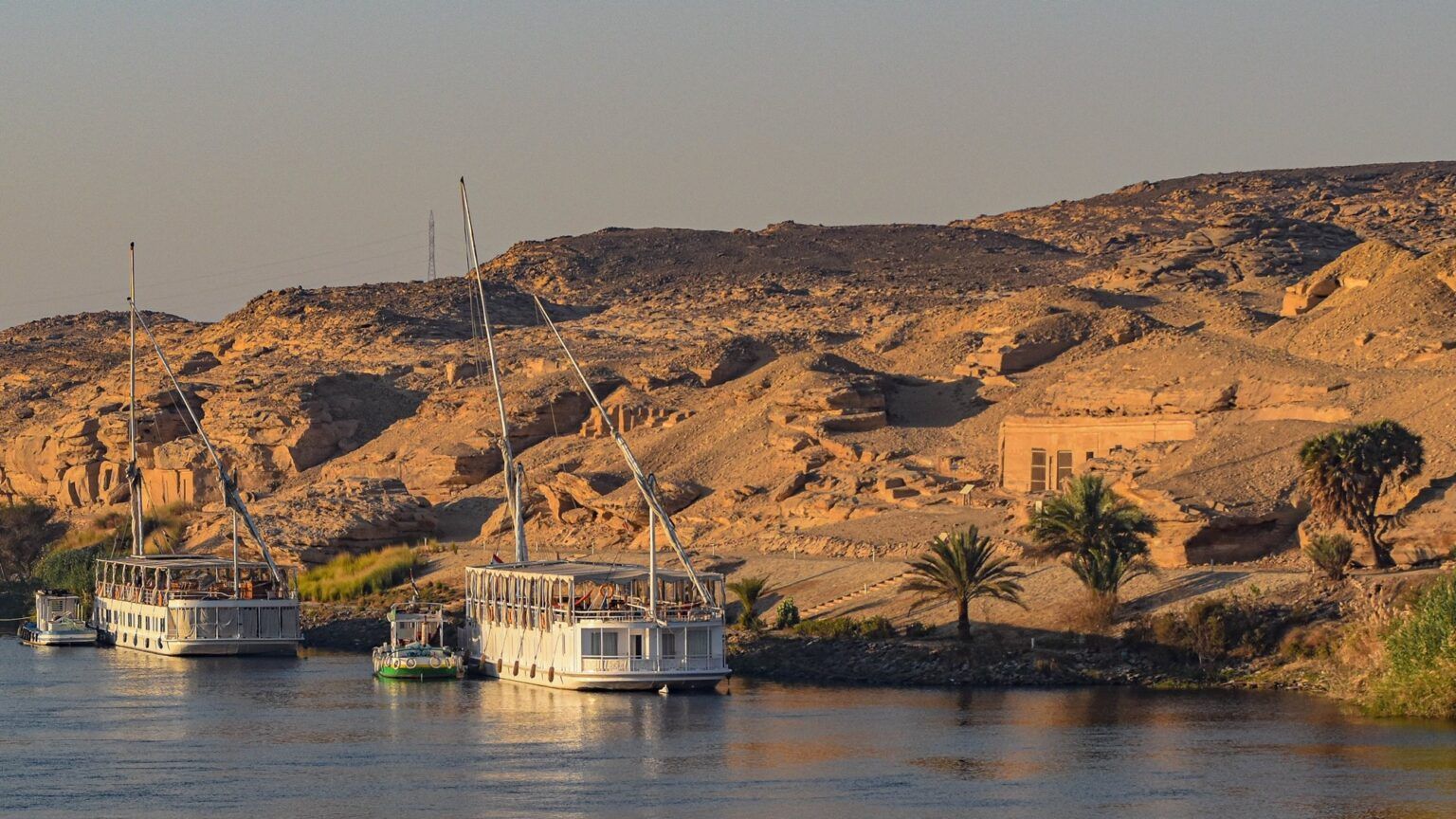 A Nile cruise ship docked in front of ancient ruins at dawn.