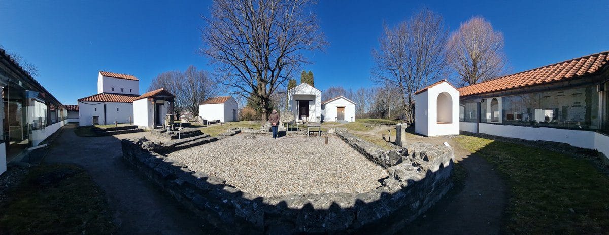 A panoramic view of part of the archaeological site of Cambodunum, showing the preserved foundations of some structures and reconstructed temples,